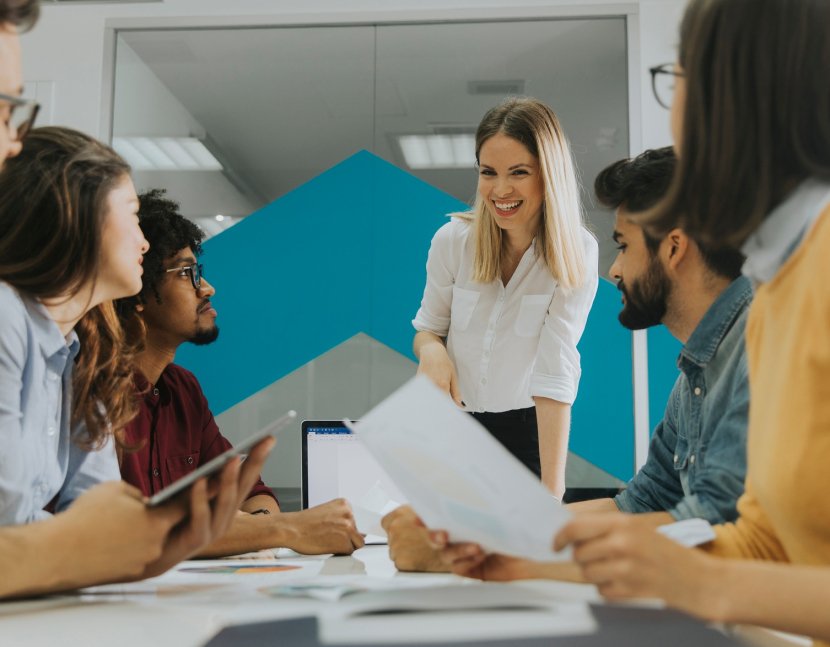 Pretty female team leader talking with mixed race group of people in the office